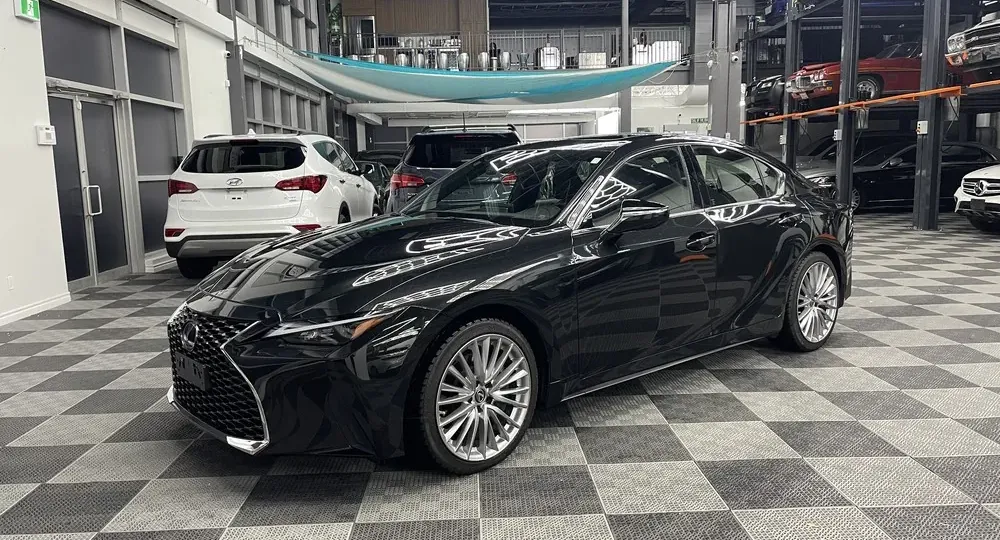 A black 2022 Lexus IS 300 on the Flat 6ix Club showroom floor, with collector cars on lifts behind it